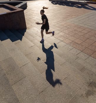 A young woman in black clothes running on stairs at city street early morning.