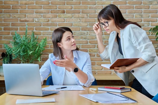 Two businesswomen talking and discussing in office. Female colleagues, manager and employee analyze and discuss documents, contracts, financial reports. Work law finance teamwork people job concept