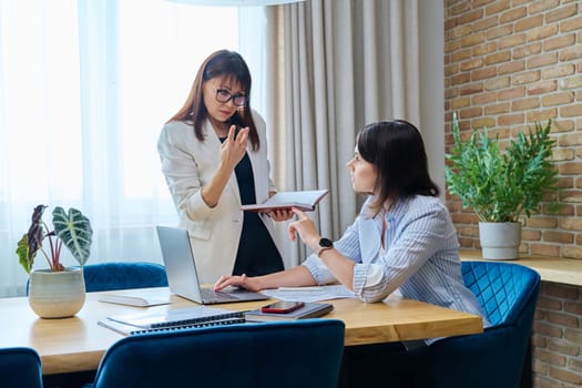 Two businesswomen talking and discussing in office. Female colleagues, manager and employee analyze and discuss documents, contracts, financial reports. Work law finance teamwork people job concept
