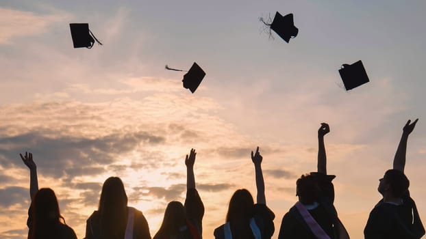 Student graduates toss their caps at sunset