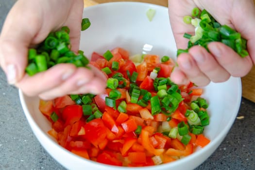 The process of preparing salad. Close-up of a woman's hands pouring finely chopped green onions into a salad. High quality photo