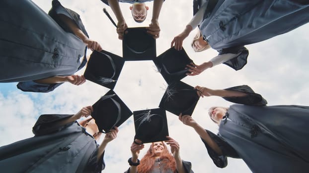 Graduates in black robes join their caps in a circle