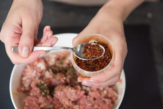 A woman's hand sprinkles ground paprika on a raw meat close-up. Freshly ground paprika is used as a raw meat dressing