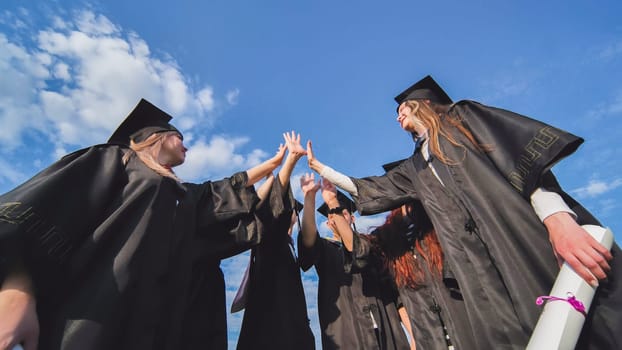 Graduates in black school uniforms join hands. The concept of team and strong friendship