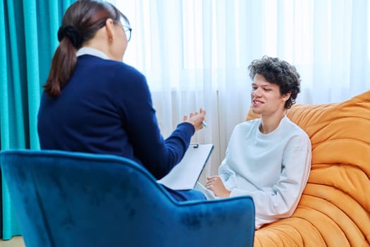 Young male having mental therapy in psychologist's office. Guy college student talking to therapist, female counselor listening talking making clipboard notes. Support psychology psychotherapy concept