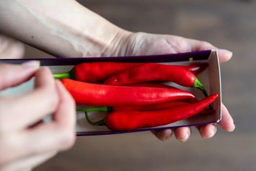 A woman's hand takes a chili pepper from a pack close-up. Start cooking a spicy soup for guests or preparing for National Chili Day. High quality photo