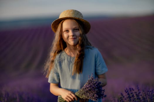 Lavender sunset girl. A laughing girl in a blue dress with flowing hair in a hat walks through a lilac field, holds a bouquet of lavender in her hands