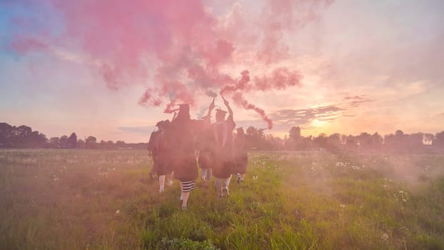 Students graduate with colored smoke walking through the meadow in the evening