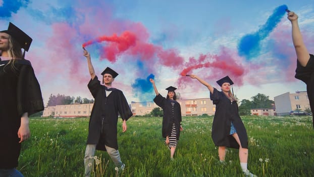 Students graduate with colored smoke walking through the meadow in the evening