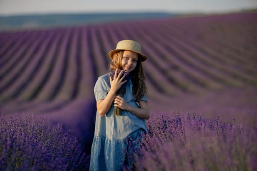 Lavender sunset girl. A laughing girl in a blue dress with flowing hair in a hat walks through a lilac field, holds a bouquet of lavender in her hands