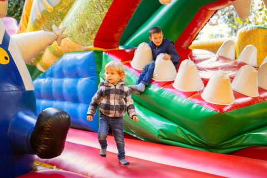 Happy kids having fun on colorful inflatable attraction playground. Children have fun and ride on the outdoor playground.