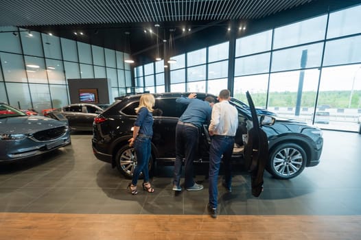 The seller demonstrates the interior of the car to buyers. Caucasian couple chooses a car