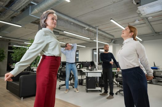 Four office workers warm up during a break. Employees do fitness exercises at the workplace