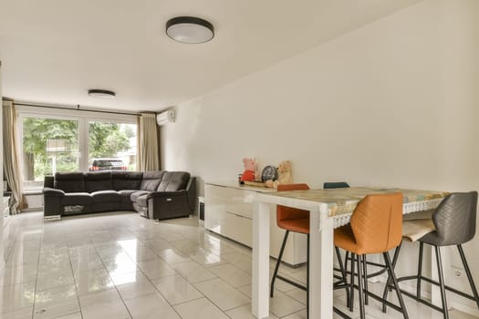 a living room and kitchen area in a house with white tile flooring, two bar stools and an open window