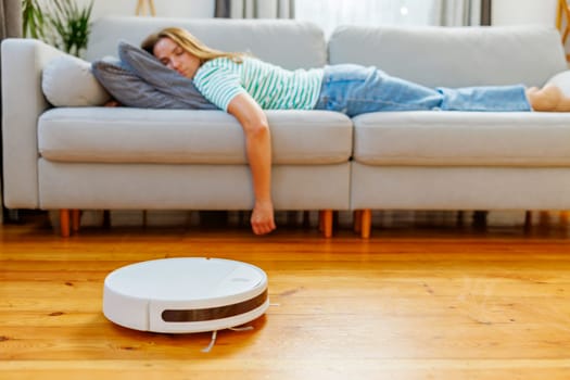 A woman peacefully sleeping on a cozy sofa while a robot vacuum quietly takes care of the cleaning. Serenity meets smart living