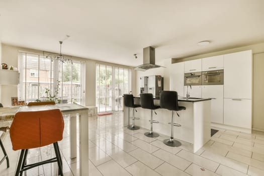 a kitchen and dining area in a house with white tiles on the floor, red bar stools and an orange chair