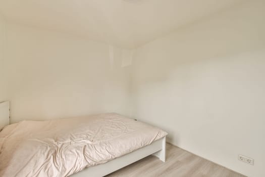 a bed in the corner of a room with white walls and wood flooring on the right side of the room