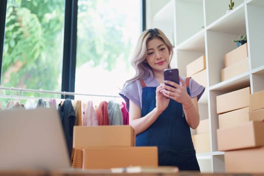 Starting small business entrepreneur of independent Asian female online seller talking on the phone with a customer and packing products for delivery to the customer. and SME delivery concept.