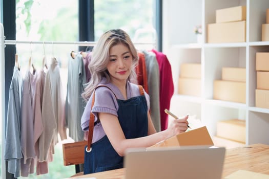 Starting small business entrepreneur of independent Asian female online seller talking on the phone with a customer and packing products for delivery to the customer. and SME delivery concept.