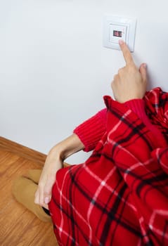 Close-up of a girl's hand in a warm plaid and woolen socks turns the floor heating thermostat to a high temperature. Setting the temperature at home
