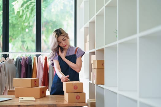 Starting small business entrepreneur of independent Asian female online seller talking on the phone with a customer and packing products for delivery to the customer. and SME delivery concept.