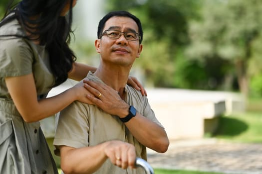 Happy middle aged asian father touching daughter hand on shoulder looking and talking together at the park.