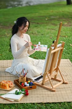 Talented young woman painting on canvas in the park. Art and leisure activity concept.