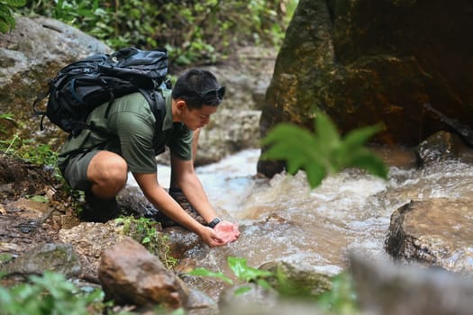 Male traveller scooping clean water in mountain stream. Travel, adventure and active life concept.