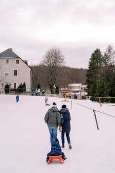 Mom and dad are carrying a small child on a sled climbing a hill. Back view. High quality photo