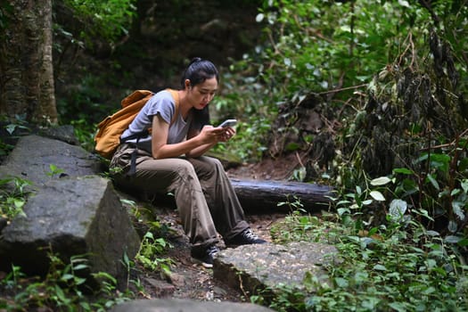 Tourist woman with backpack using mobile phone in forest. Travel, vacation and adventure concept.