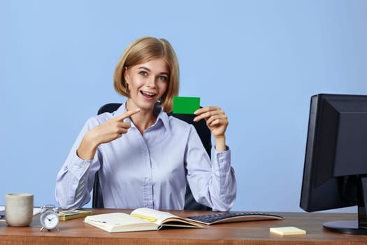 attractive blonde businesswoman pointing at plastic credit card on blue background