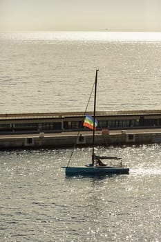 Monaco, Monte Carlo, 23 October 2022: sailing boat with lgbt flag leaves the port Hercules at sunset, the team prepares the boat, pier and mega yacht. High quality photo