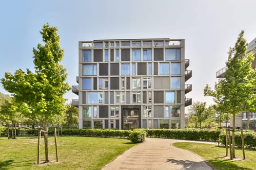 a building with many windows and trees in the front yard, on a sunny day at an urban city park