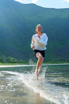 Young girl teenager running on beach in Norway Fjord. Vacation in Nordland in summer.