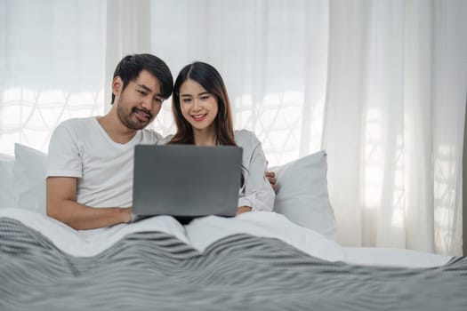 Photo of happy young couple using laptop while relaxing on bed at home..
