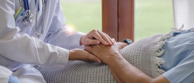 close up, an elderly male patient holds hands with a nurse who comes to take care of and help encourage each other..