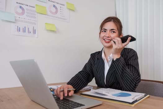 Asian businesswoman in a formal suit in the office is happy and cheerful while using a smartphone to work in her office..