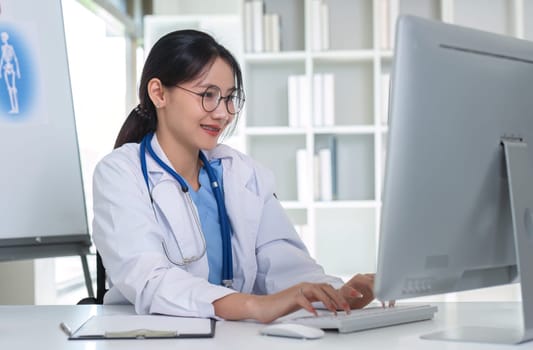 Young Asian doctor in a white medical uniform with a stethoscope using a lab computer and tablet to organize and classify medicines in preparation for administration to patients..