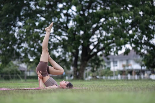 Young healthy Asian woman stretch her body on a yoga mat. Do yoga in a lush park Yoga and Pilates concept.