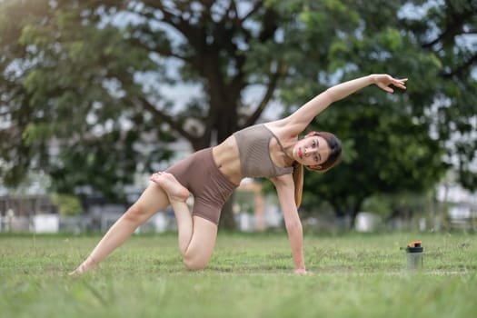 Young healthy Asian woman stretch her body on a yoga mat. Do yoga in a lush park Yoga and Pilates concept.