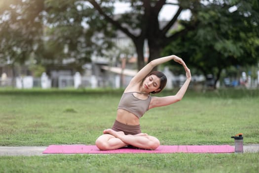 Young healthy Asian woman stretch her body on a yoga mat. Do yoga in a lush park Yoga and Pilates concept.