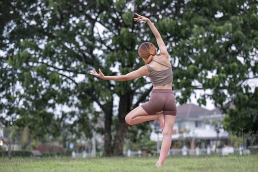 Young healthy Asian woman stretch her body on a yoga mat. Do yoga in a lush park Yoga and Pilates concept.