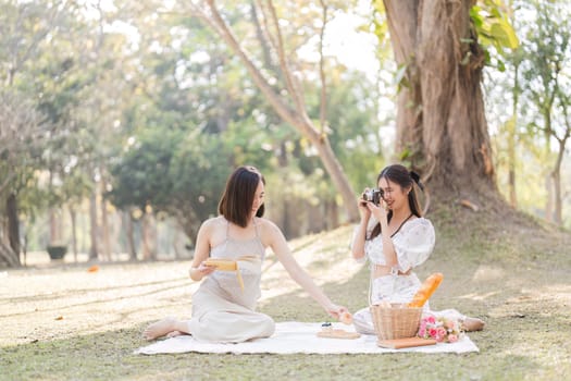 Two beautiful LGBT young women in casual clothes and summer hats Carefree woman having a picnic outside Positive model sitting on the grass eat fruit and cheese Take a selfie. LGBT concept.