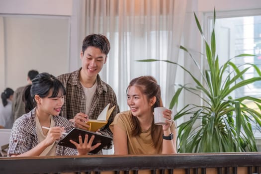 A happy young Asian man and a pretty girl are study on a tablet together, study on a co-project, sharing ideas and discussing work in a room..