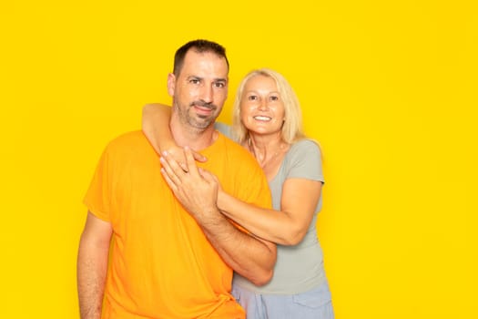 White happy couple hugging and looking at camera isolated over yellow background