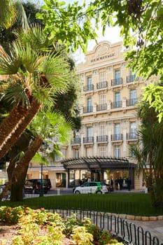 Monaco, Monte-Carlo, 09 November 2022: The Hotel Hermitage through flowers at sunny day, luxury life, building exterior of famous hotel, palm trees, sunshine, balcony. High quality photo