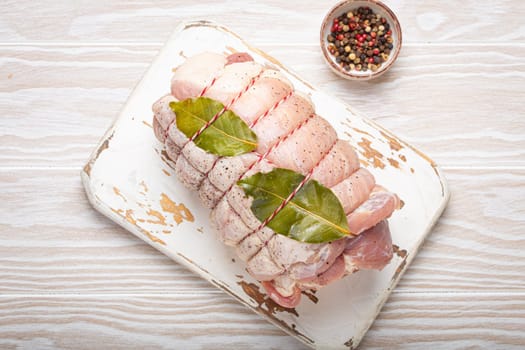 Raw wrapped rolled sliced pork with bay leaf and seasonings on white cutting board on rustic white wooden background top view. Pork roll ready to be prepared.