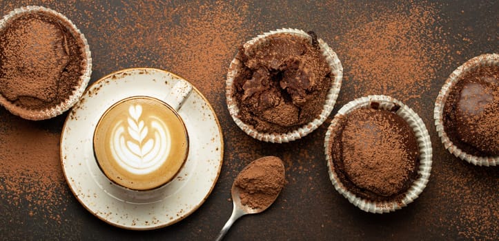 Chocolate and cocoa browny muffins with coffee cappuccino in cup top view on brown rustic stone background, sweet homemade dark chocolate cupcakes.