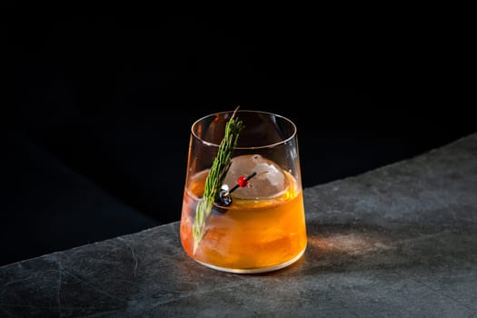 orange alcoholic cocktail with a sprig of pine needles and round ice