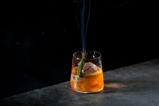 orange alcoholic cocktail with a sprig of pine needles and round ice